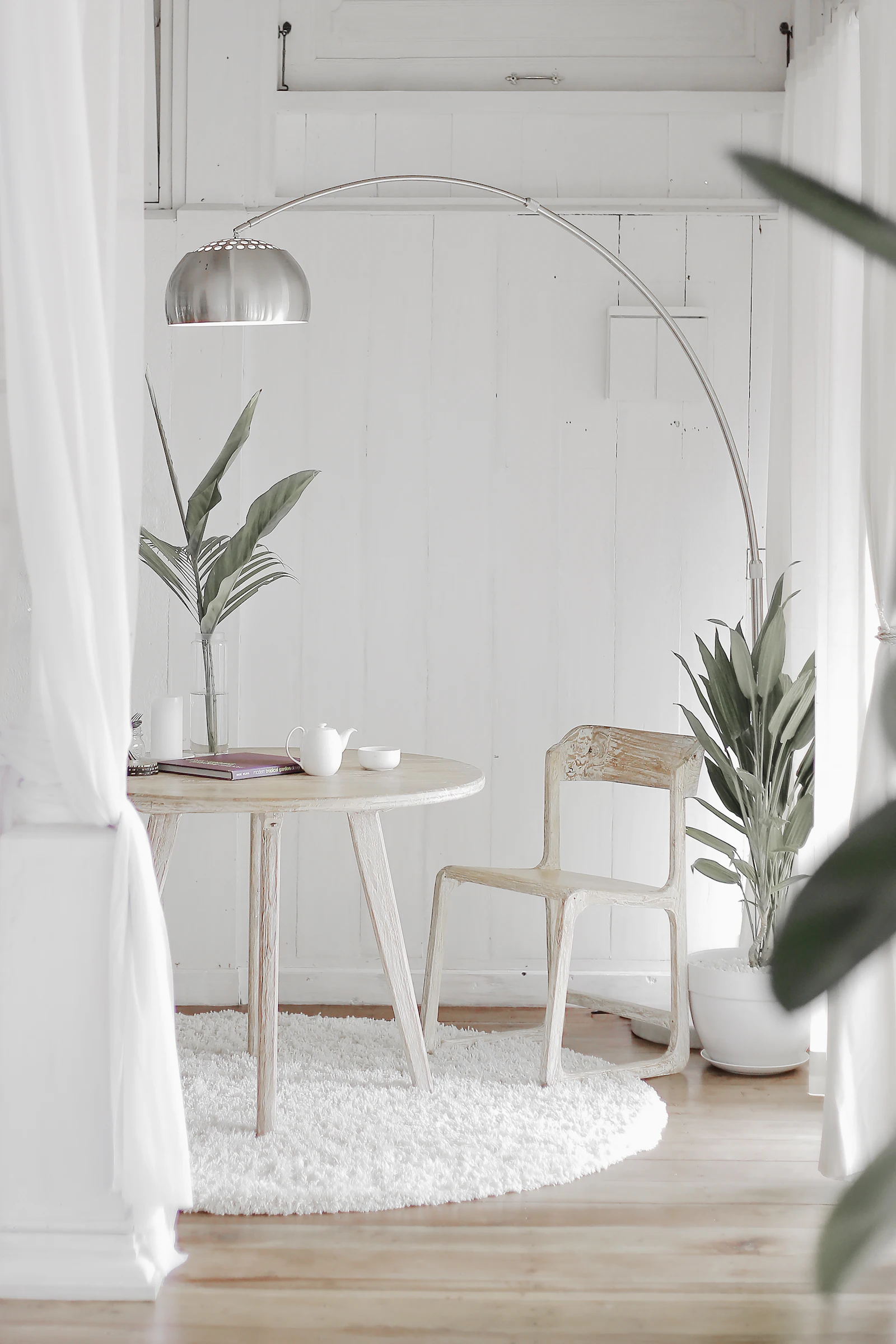 Rincón de lectura con mesa de madera encalada, lámpara de arco y plantas