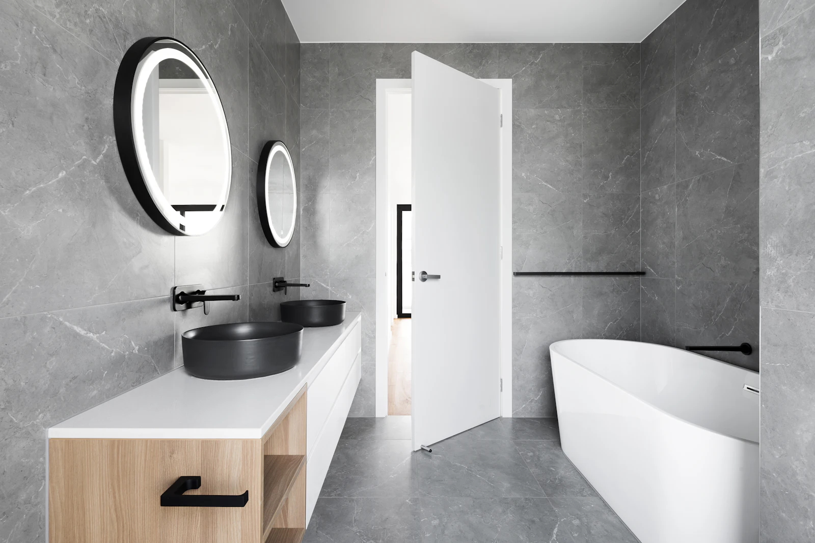 Baño principal de Casa Tolosa con piedra gris, lavabos negros y mueble de roble